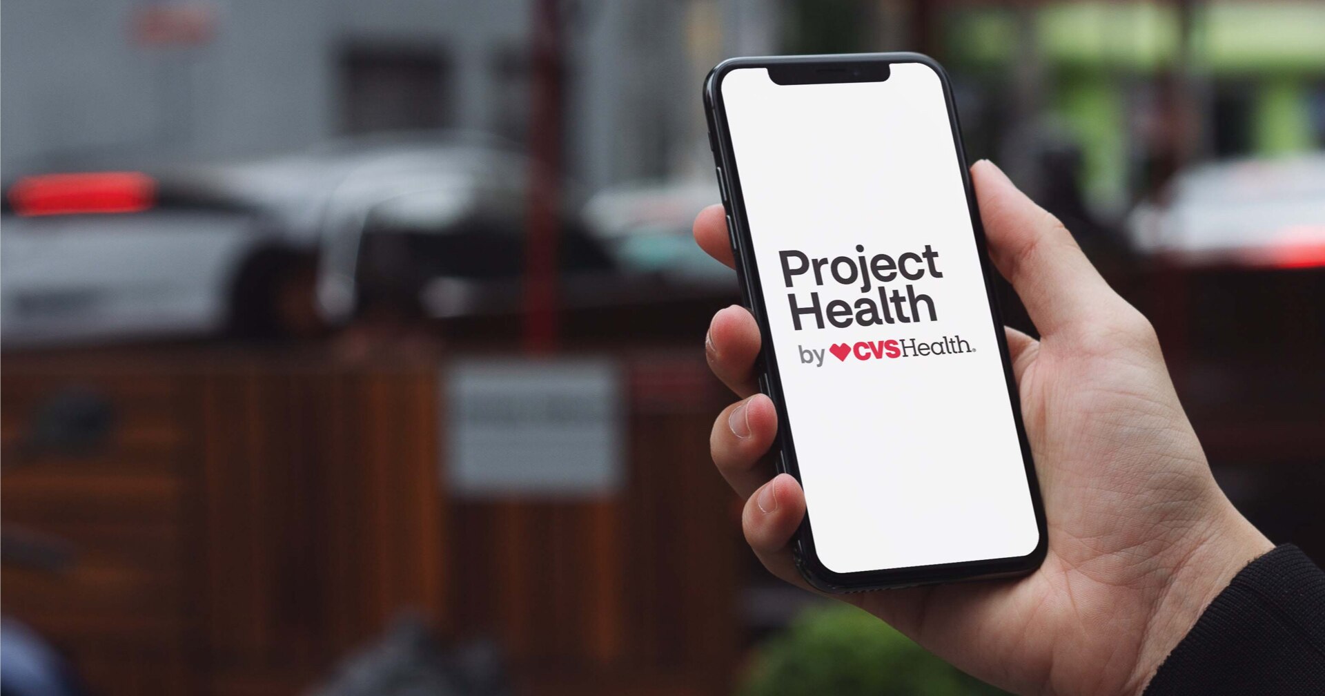 A hand holding a mobile device with the words Project Health by CVSHealth on its screen
