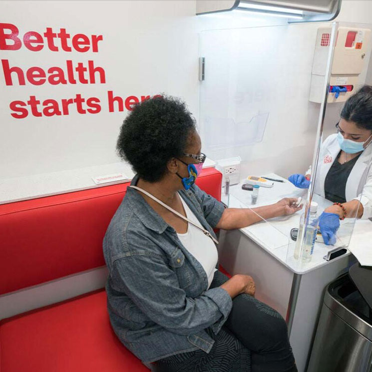 A woman wearing a face covering, getting a health screening from a clinician