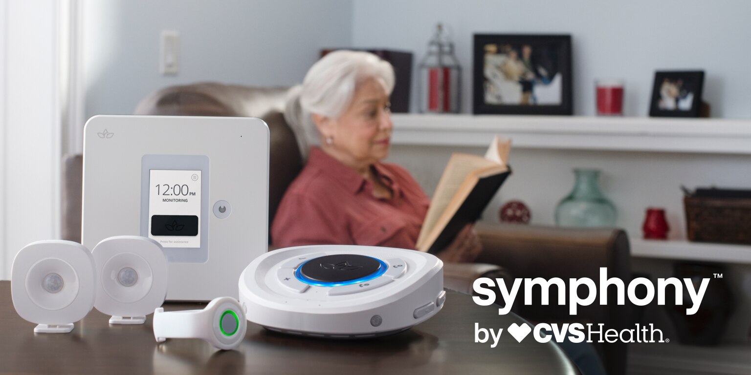 A senior citizen reads a book in her living room with her Smart Hub on the side table.