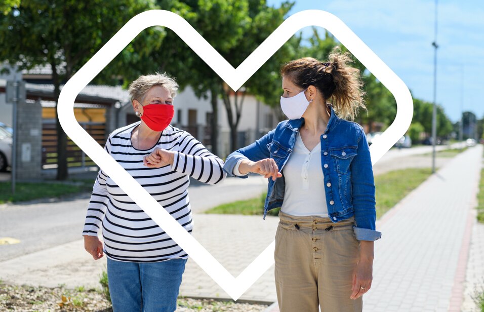 An image of two women in face coverings bumping elbows