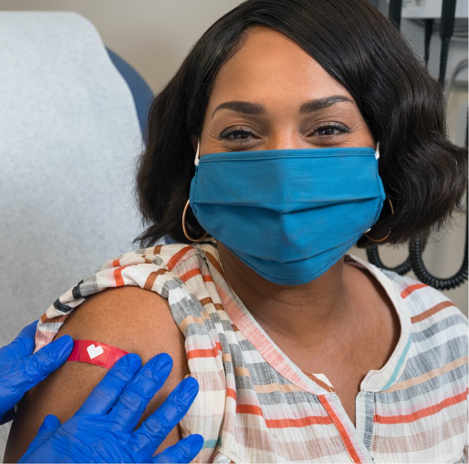 Imagen de una mujer con una cubierta para la cara que sonríe mientras un trabajador de la salud le pone una venda luego de haberle aplicado la vacuna contra el COVID-19.