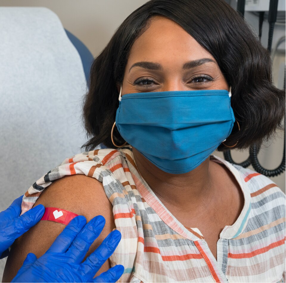 image of woman in a face covering smiling while healthcare worker applies a bandage after COVID-19 vaccination