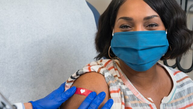 Imagen de una mujer con una cubierta para la cara que sonríe mientras un trabajador de la salud le pone una venda luego de haberle aplicado la vacuna contra el COVID-19.