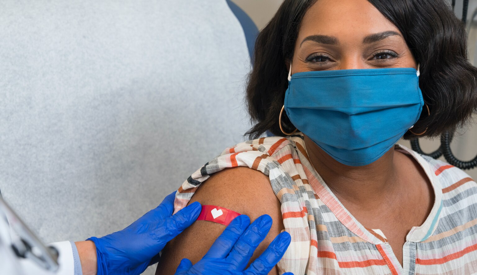 Imagen de una mujer con una cubierta para la cara que sonríe mientras un trabajador de la salud le pone una venda luego de haberle aplicado la vacuna contra el COVID-19.