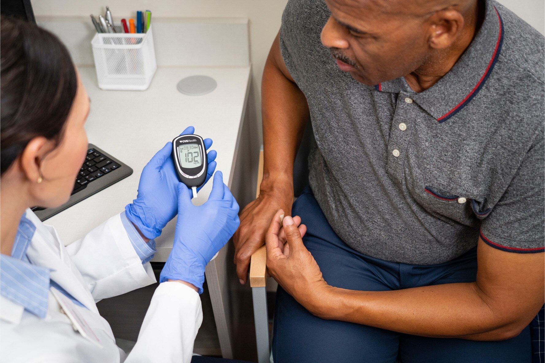 A MinuteClinic provider is explaining the reading on a glucometer to her patient in a clinical setting.