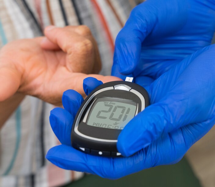 Un profesional de cuidado de la salud utiliza un glucómetro para verificar el azúcar en la sangre de un paciente.