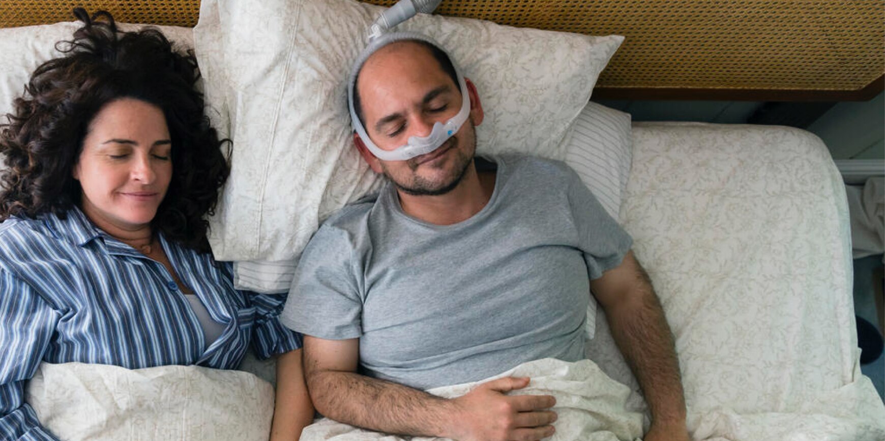 A couple sleeping peacefully in bed, where one person is wearing sleep apnea medical equipment.