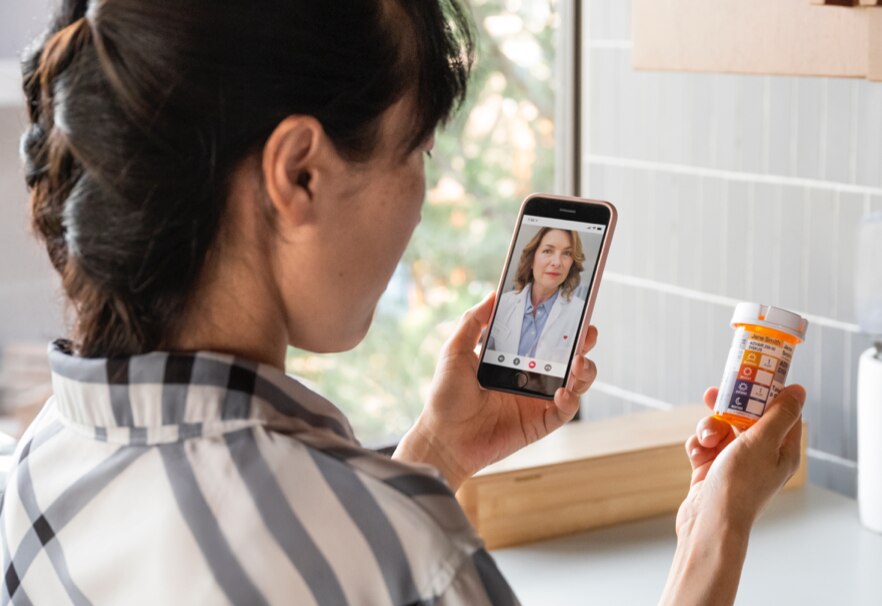 Mujer sentada en un sofá interactuando con un profesional de la salud en una tablet durante una consulta de telesalud. Conozca más sobre MinuteClinic ahora.