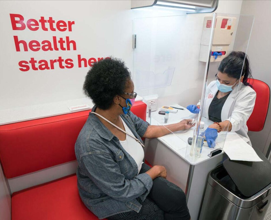 A woman wearing a face covering, getting a health screening from a clinician