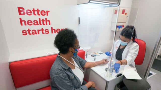 A woman wearing a face covering, getting a health screening from a clinician