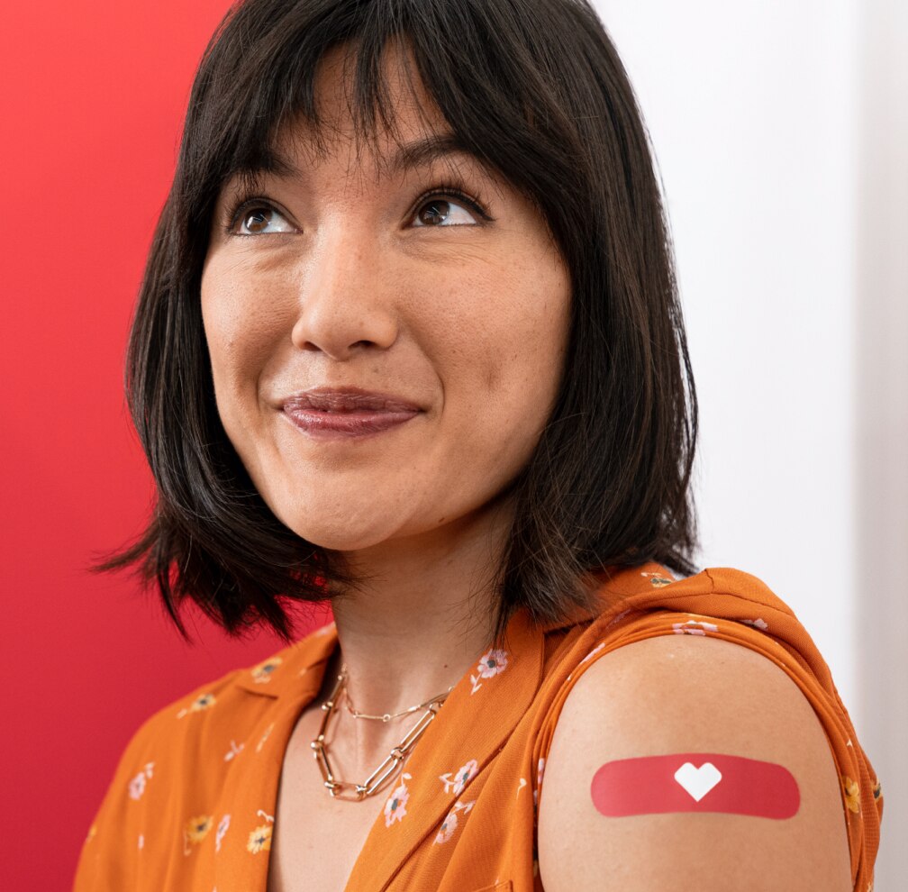 Foto de cabeza y hombros de una paciente sonriente que acaba de vacunarse. En su brazo hay un apósito de CVS rojo.