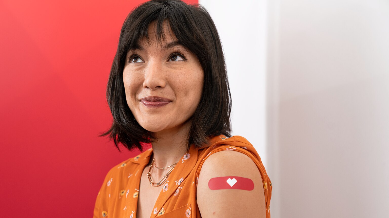 Head and shoulder photo of smiling female patient who has just received her vaccination. There is a red CVS bandage on her arm.