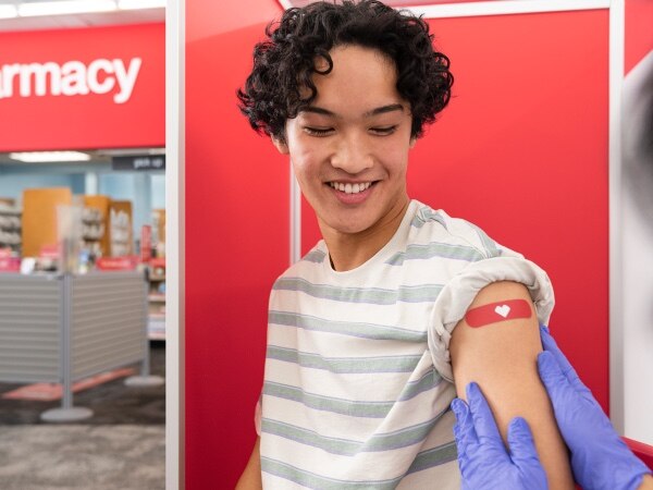 Smiling young person receiving red CVS heart bandage on arm after flu shot