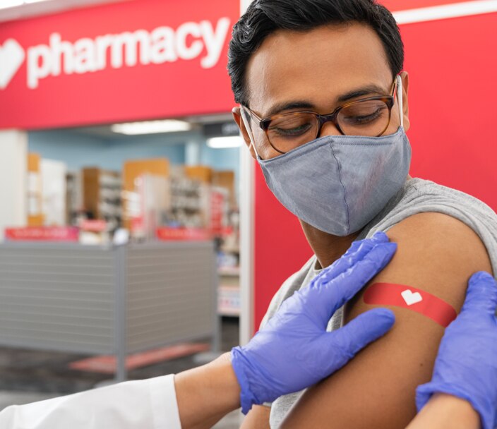 Hombre joven con una mascarilla protectora puesta y apósito CVS en el brazo después de haber recibido una vacuna contra la gripe