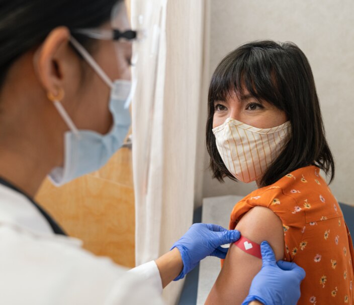 Young girl with mask on in MinuteClinic exam room having CVS band-aid applied to her arm after receiving flu shot