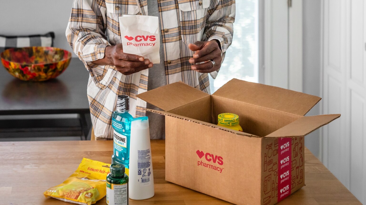 Hombre en casa abriendo caja de entrega de CVS con artículos de uso cotidiano y medicamentos con receta
