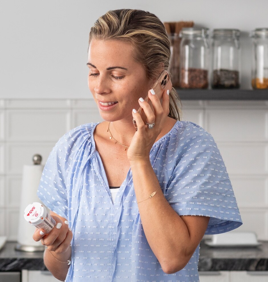 Woman at home talking on phone holding a CVS prescription bottle.