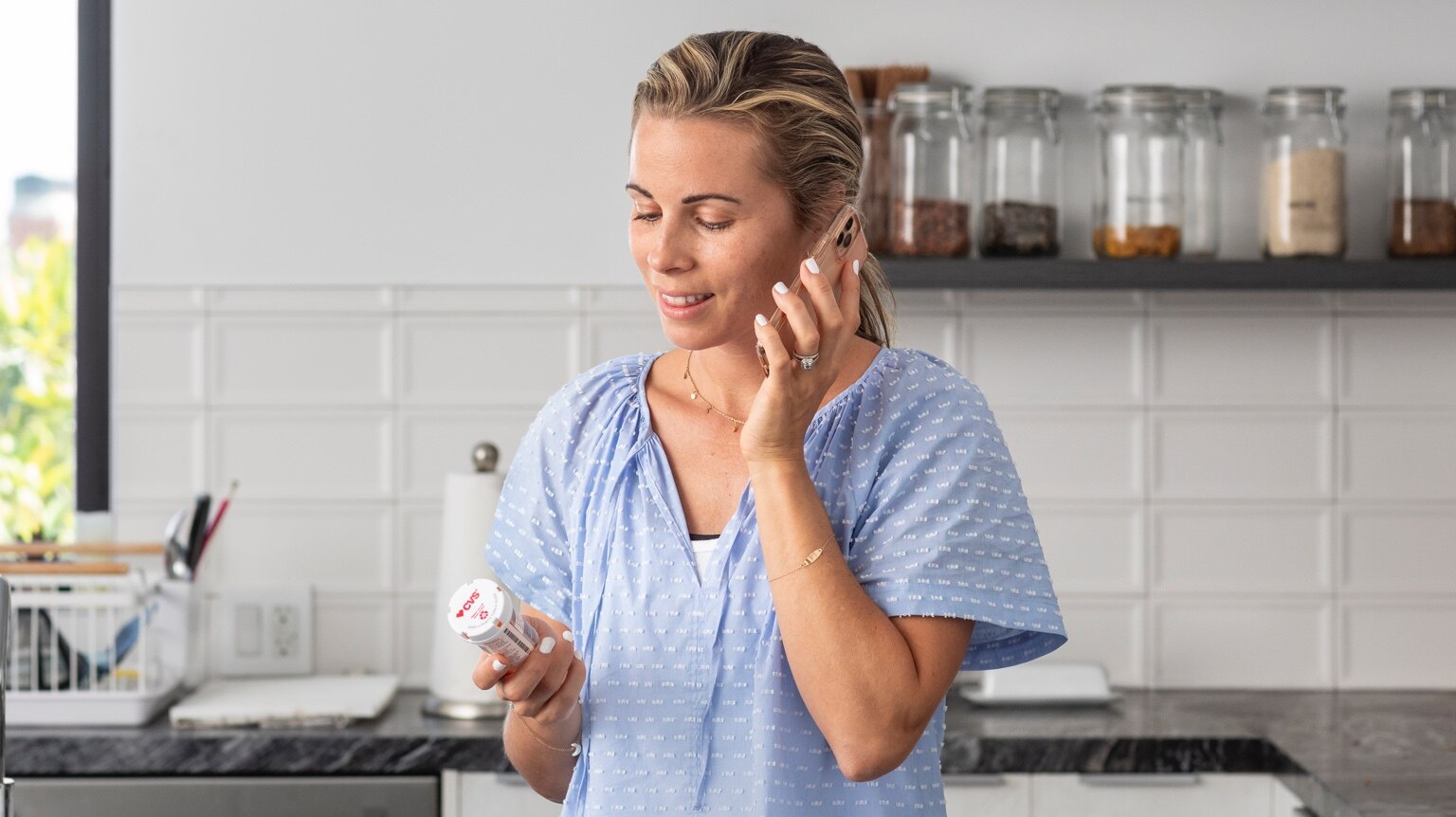 Mujer en casa hablando por teléfono con un frasco de medicamento con receta de CVS en la mano.