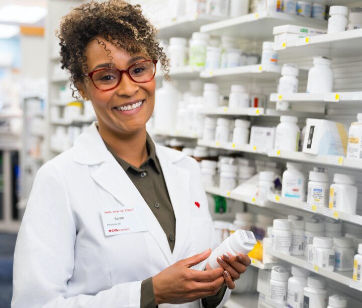 Helpful pharmacist holding prescription bottle with shelves of medication in background