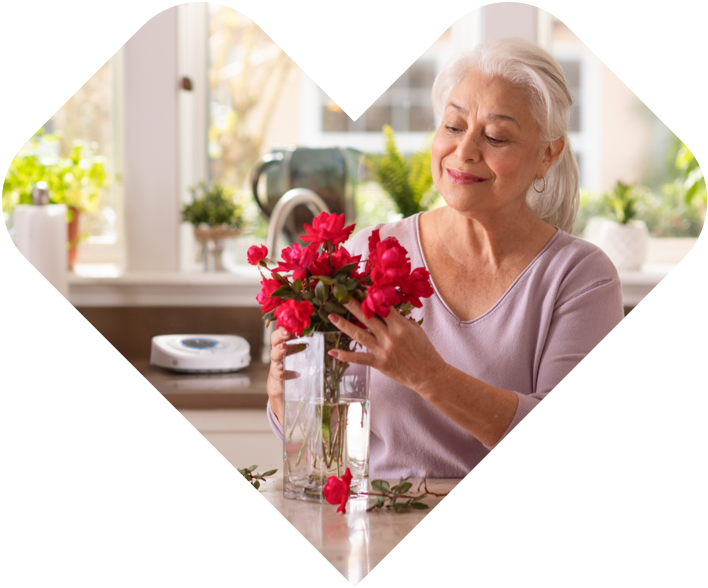 Smart Hub located on kitchen counter in the back, while senior woman is preparing a bouquet of flowers and putting them in a vase on the kitchen island.