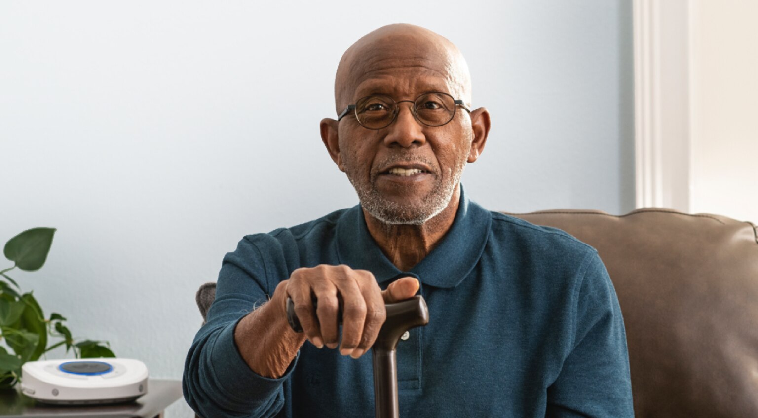 Smart Hub out of focus on living room side table. Elder gentleman sitting on couch holding walking cane.