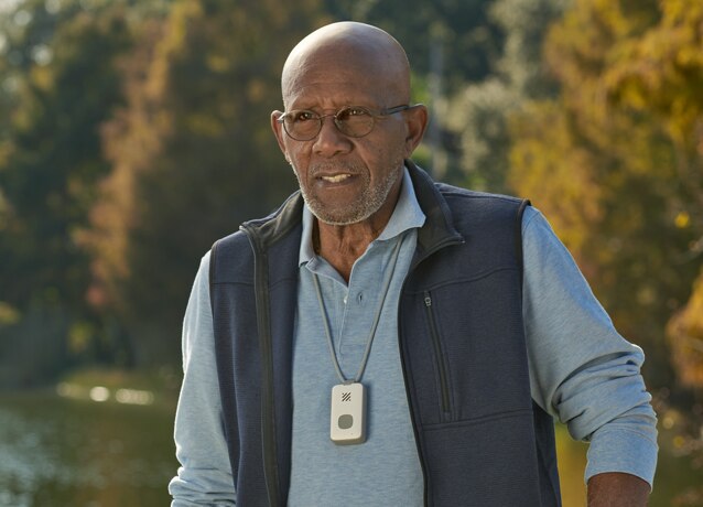 Senior man walking by a lake wearing mobile companion