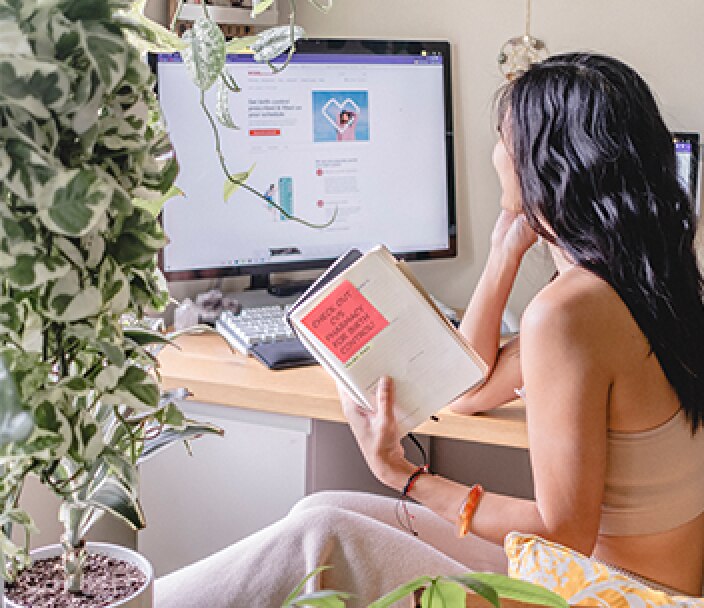 La influencer de Instagram @bylisalinh sentada frente a una computadora con la página web de salud femenina en pantalla y un cuaderno en la mano.