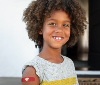 A young smiling girl with a CVS heart bandage on her arm, after being vaccinated