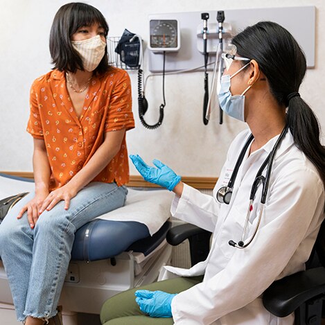 A woman speaking with her doctor, both wearing face coverings