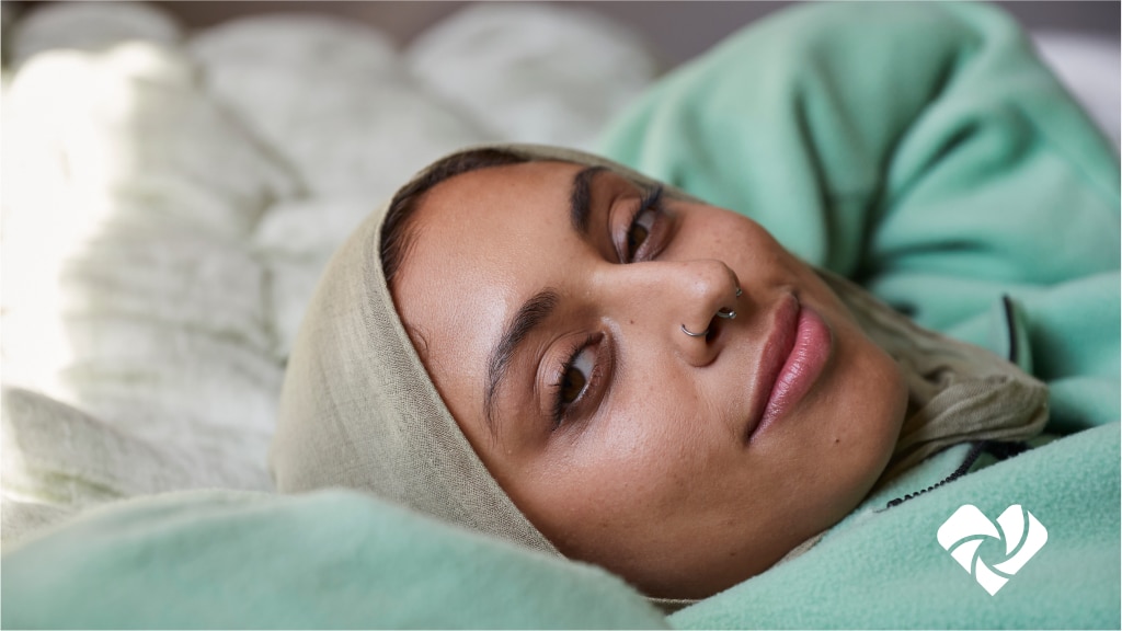 A woman wearing a hijab lies on a bed while looking at the camera.