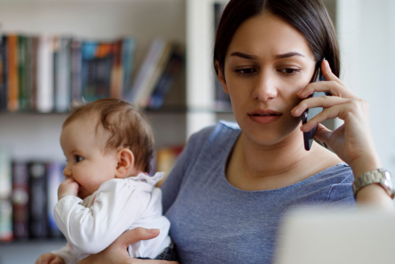 A mother talks on the phone while holding her baby in one arm.