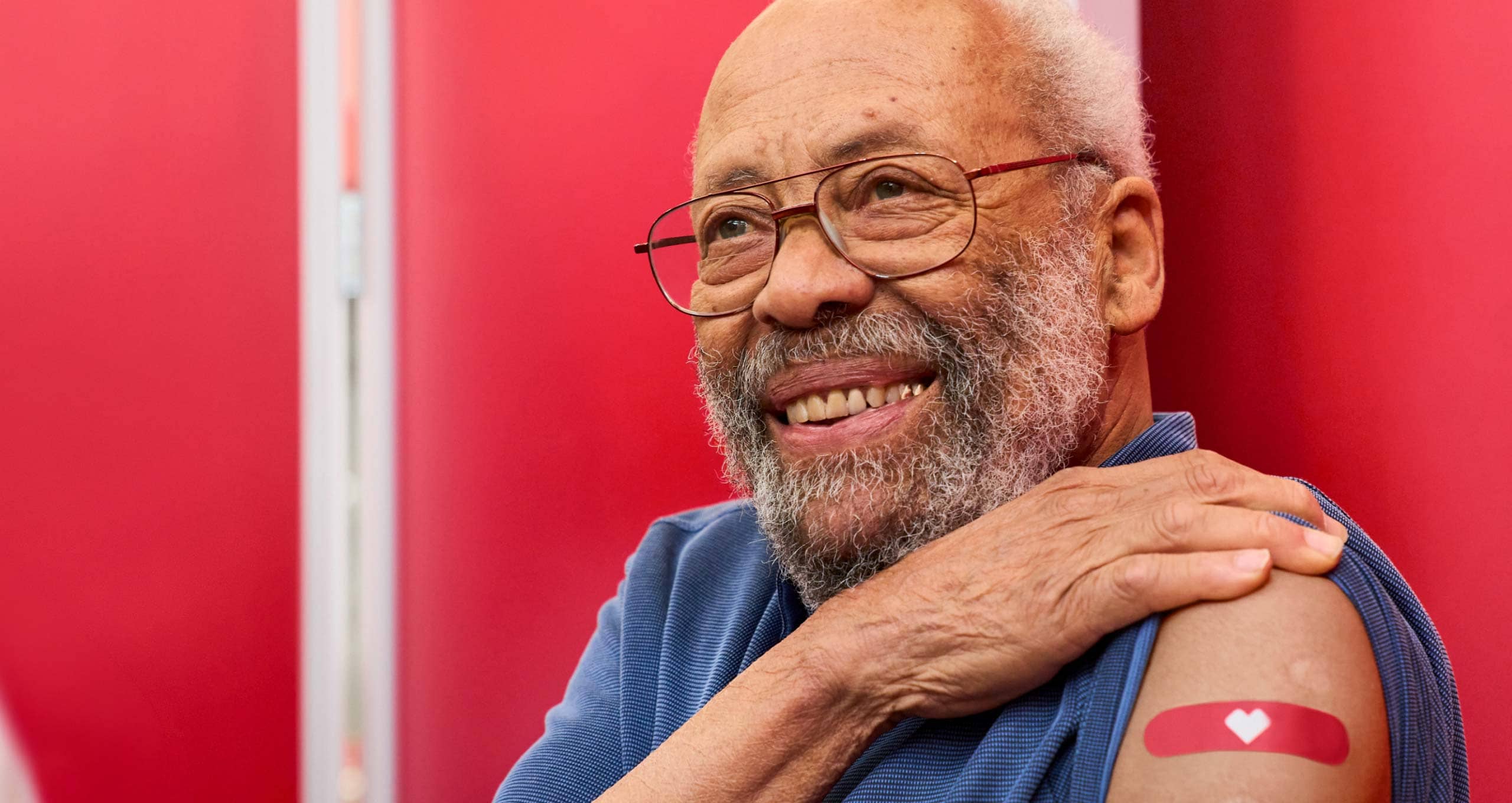 An older patient smiles and proudly rolls up his sleeve to show off his CVS bandaid after protecting his health with a no-cost vaccine with Medicare.