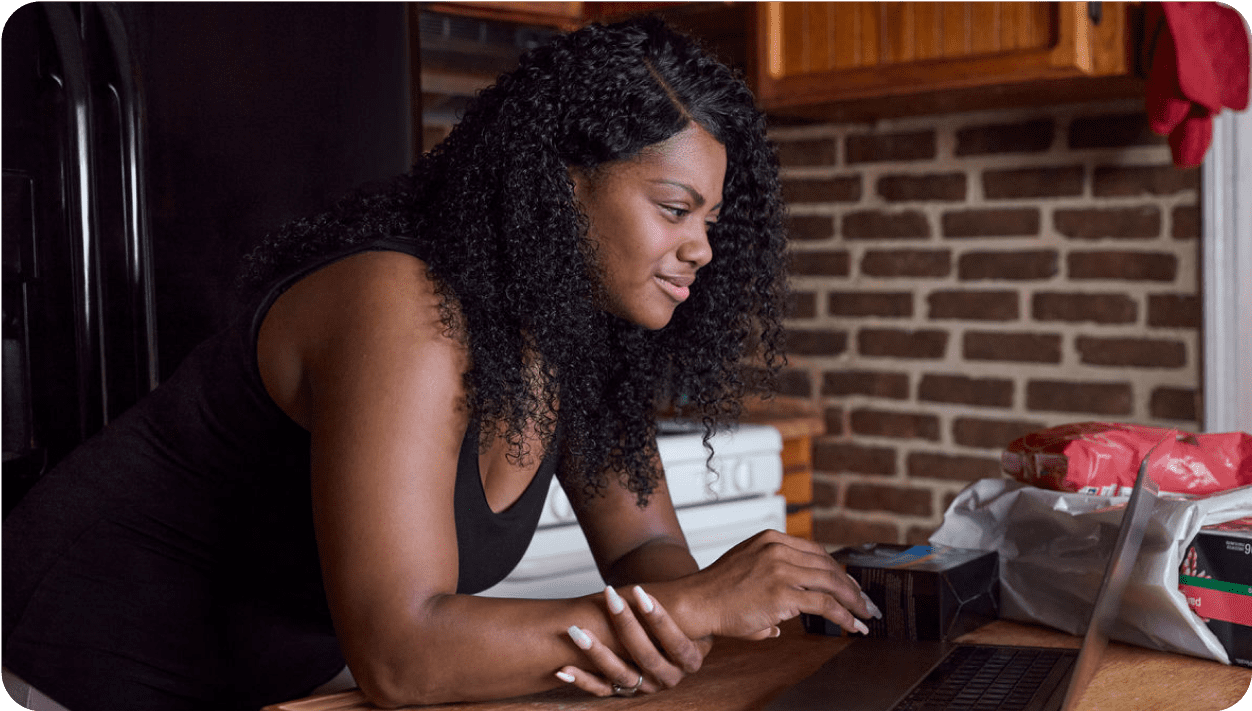 young woman of color reads period information on her laptop.