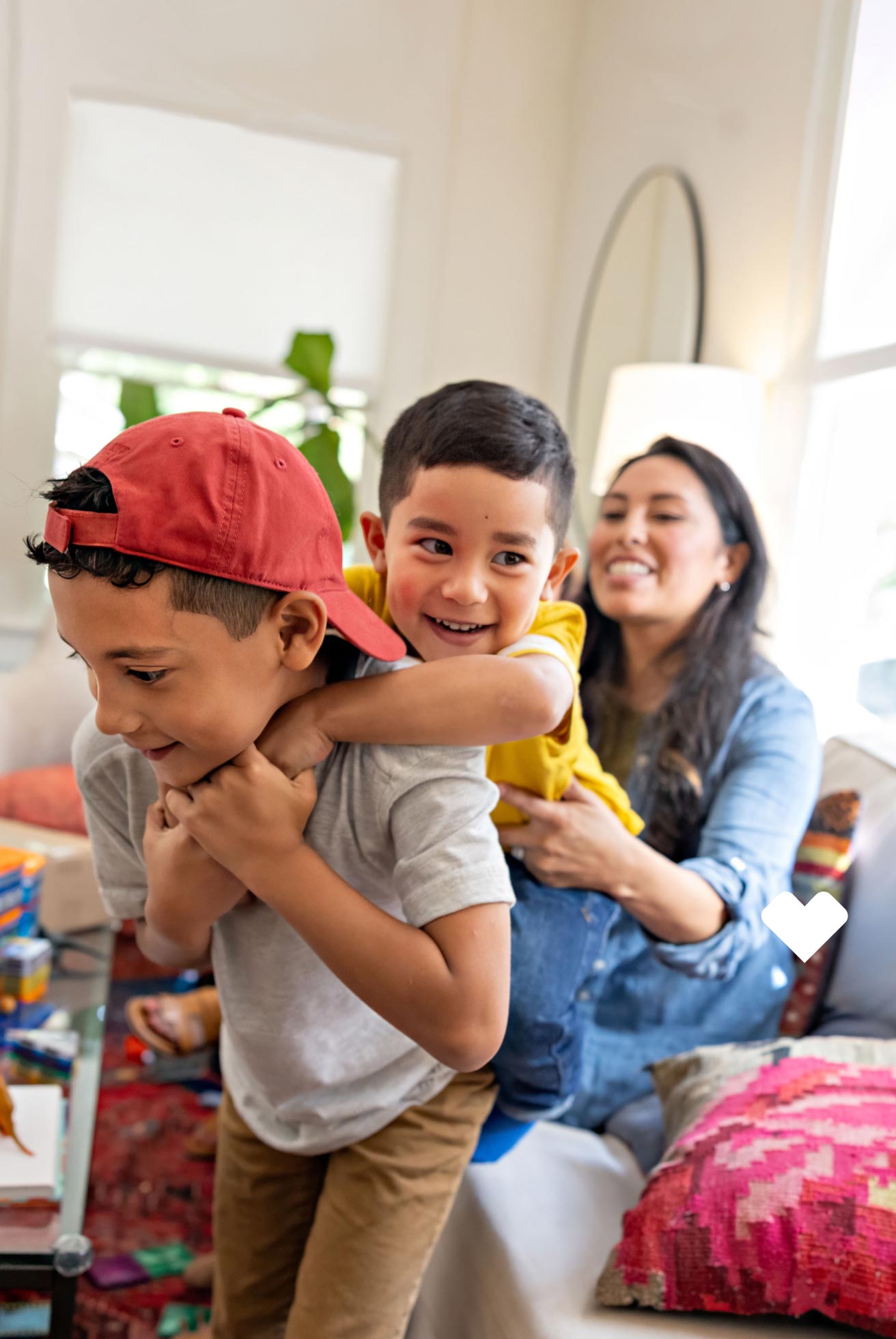 Little boy carrying his smaller brother around the living room as their mom looks on
