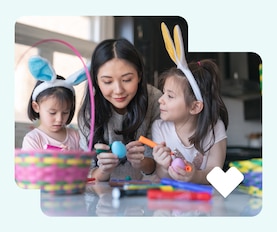 Two kids wearing bunny ears decorate Easter eggs with their parent.