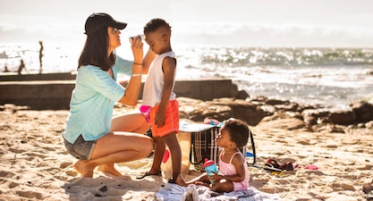 A parent applies sunscreen to their child's face at the beach.