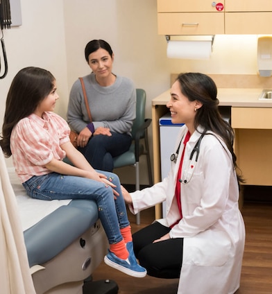 A child talks with a health care provider while their parent smiles at them.