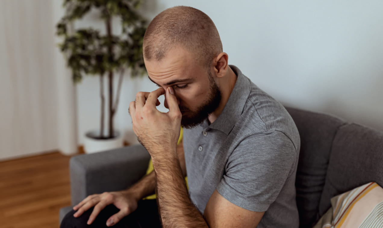 A person sits with their thumb and forefinger pressed to the bridge of their nose.