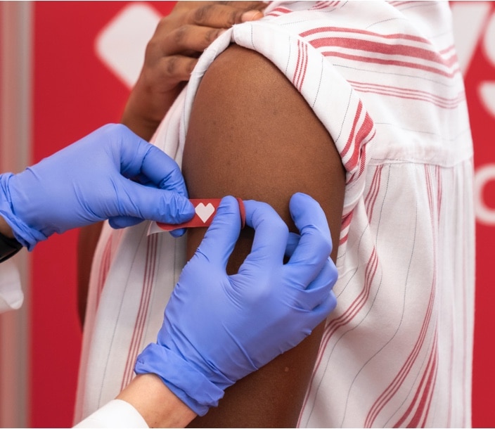 Brazo de una persona recién vacunada recibiendo una venda roja de CVS