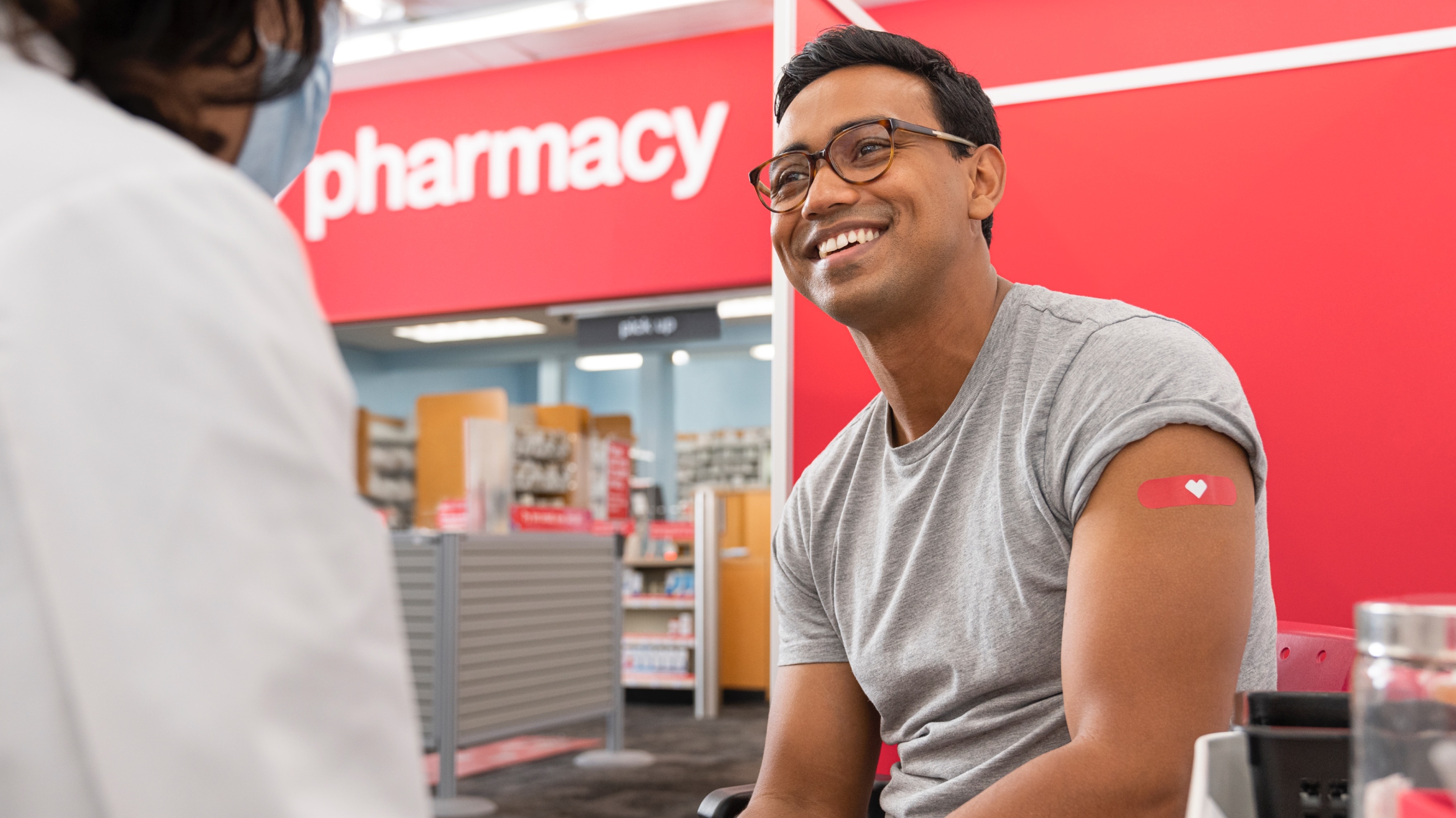Un joven sonriendo en la farmacia con el apósito rojo de CVS en el brazo después de recibir la vacuna