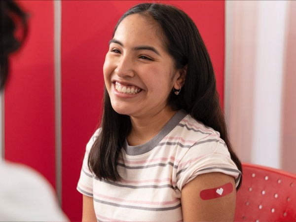Una adolescente sonriendo con el apósito rojo de CVS en el brazo después de recibir la vacuna