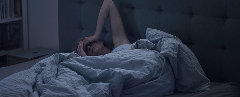 A person lies in bed and wipes sweat off their brow during the night.