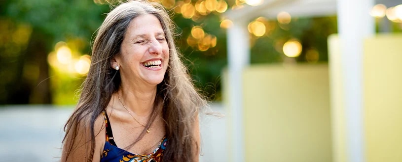 Healthy, mature woman with dark, grayless hair smiles at the camera in a floral outdoor setting.