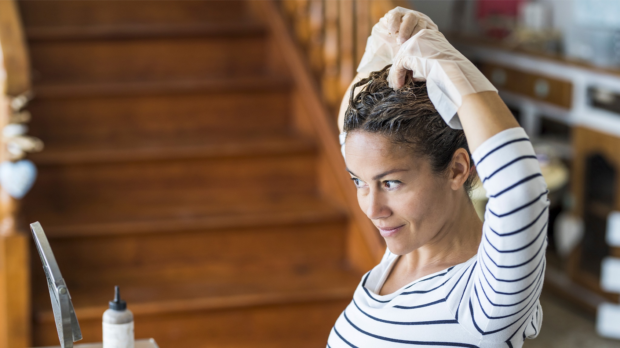 Young woman looks in a mirror while applying an at-home hair dye.