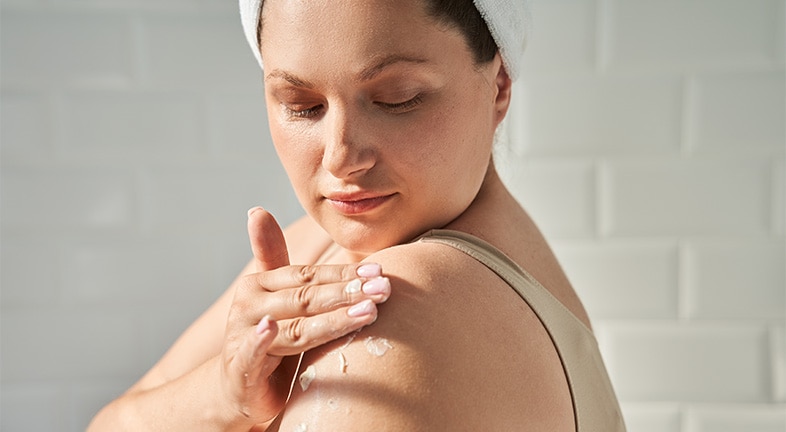Woman applying lotion containing hyaluronic acid to dry skin on her upper arm.