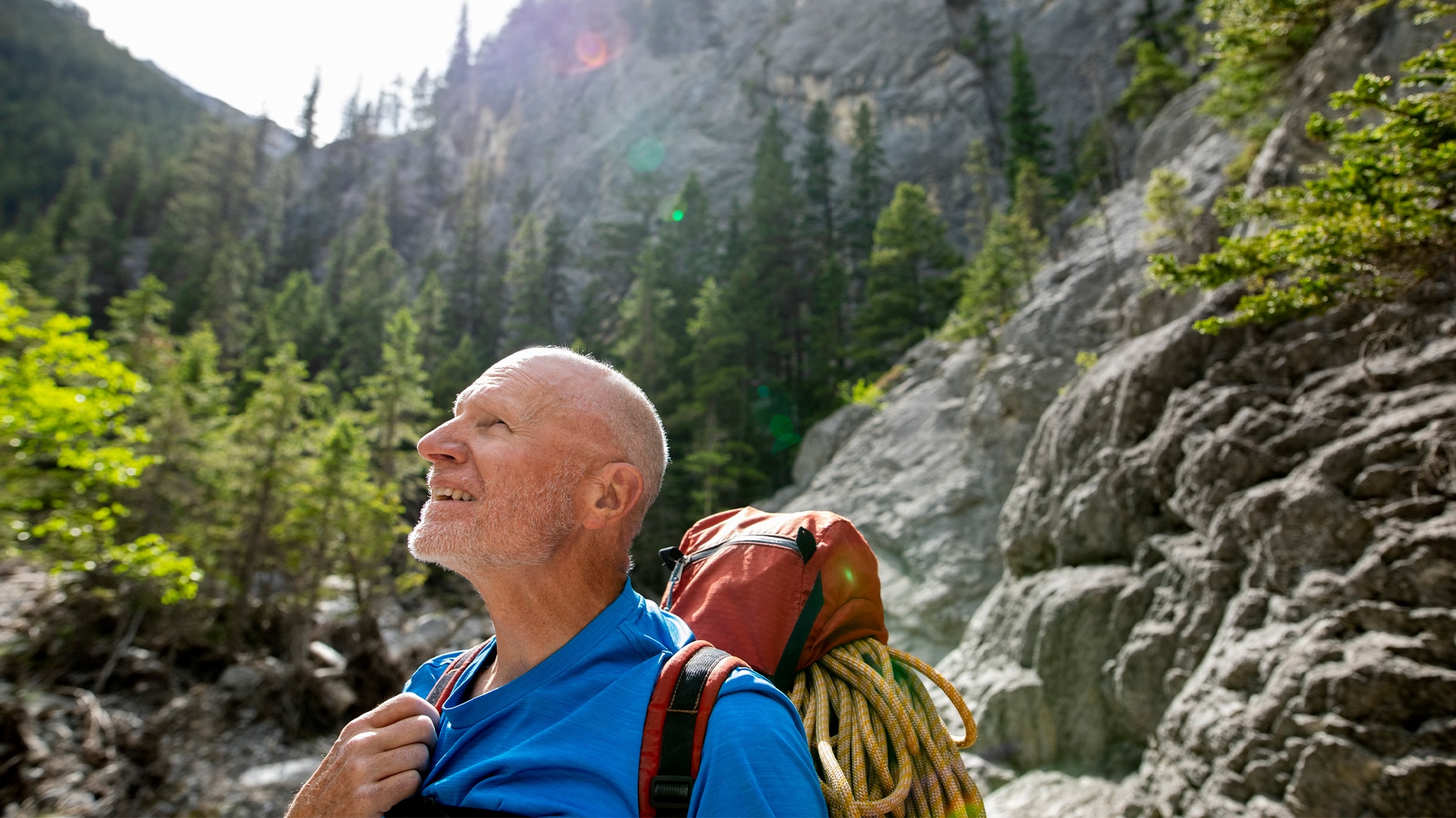 Healthy, mature man standing in the sunny woods carrying a hiking backpack.