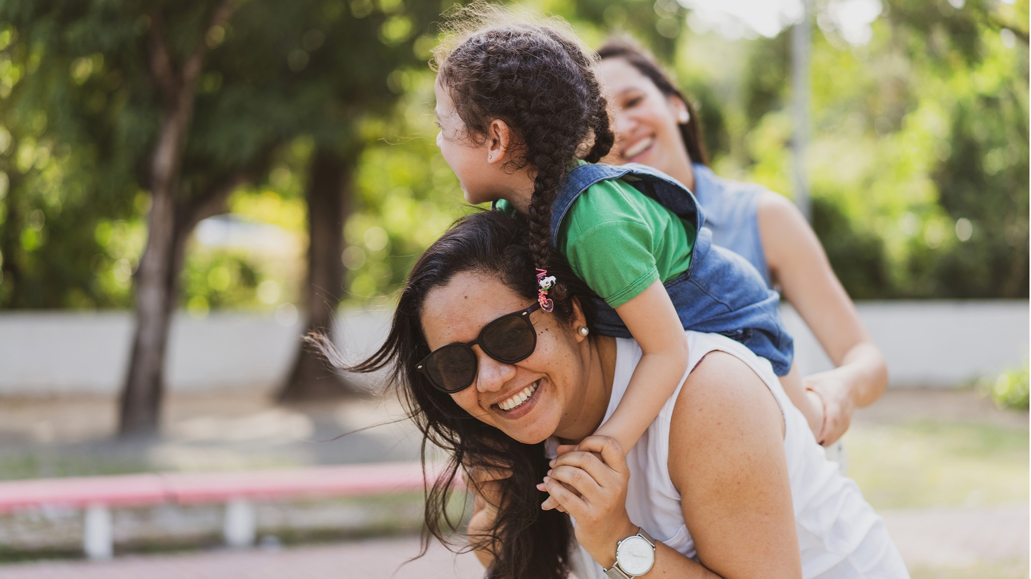 Mom carrying her daughter on her shoulders while laughing in a wooded park.
