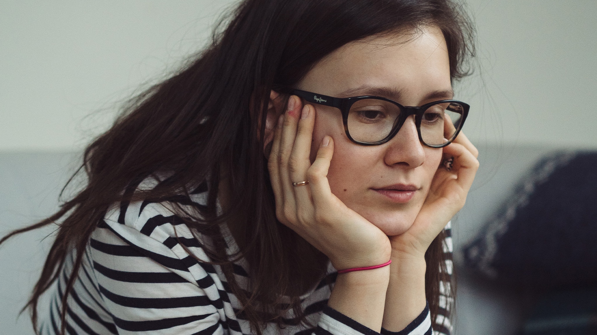 Young woman with glasses sitting with her head in her hands.