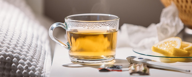 Hot tea with honey and lemon on a bedside table.