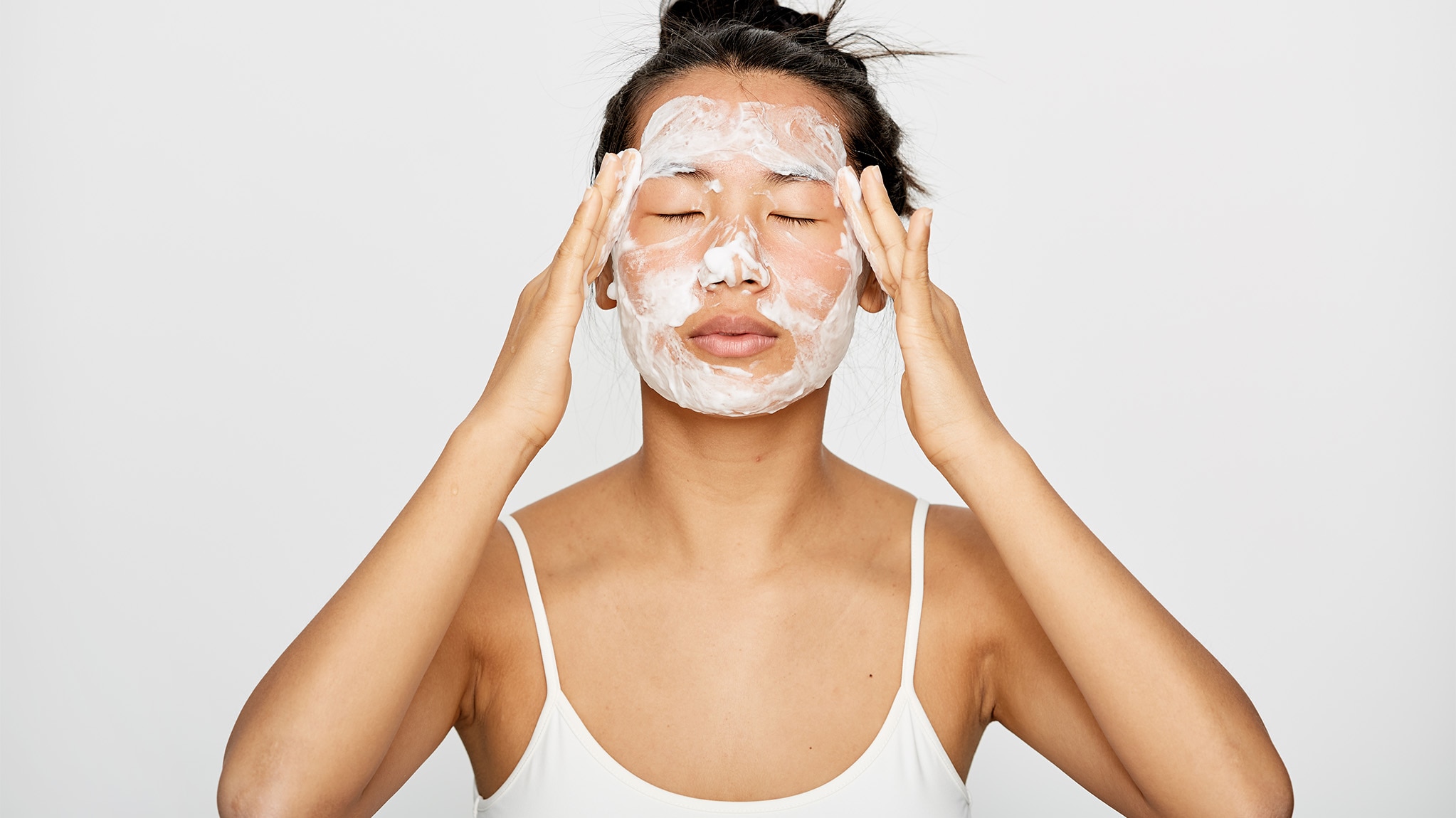 Young woman applying facial cleanser.